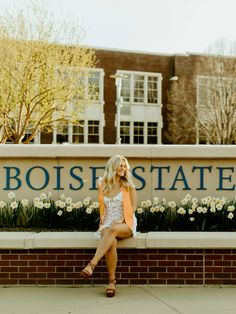 a blonde woman sitting on a brick bench in front of the boise state university sign