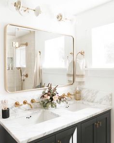 a white bathroom with marble counter tops and gold faucets on the mirror above it