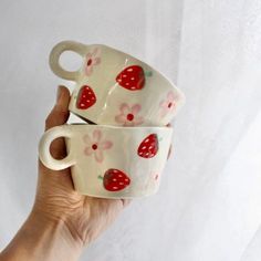 two coffee cups with strawberries on them are held up in the air by a hand