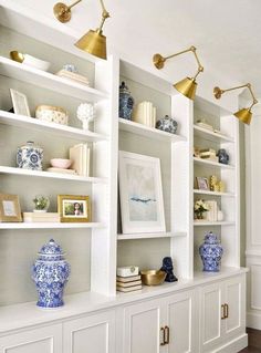 a white bookcase with blue and white vases on it's shelves in a living room