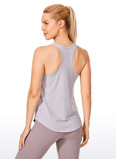 a woman in grey tank top and leggings looking down at her back with one hand on her hip