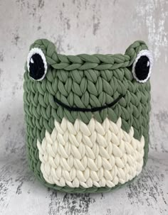 a crocheted frog basket with eyes on it's face, sitting on a white surface