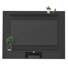 a black wall mounted tv with a plant on it's shelf next to a remote control