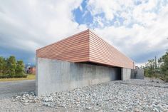 a concrete building with a wooden roof on top of gravel covered ground next to trees