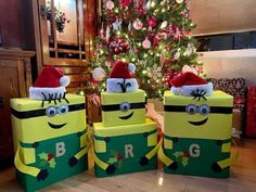 three boxes with christmas decorations on them sitting in front of a christmas tree, one is wearing a santa hat and the other has eyes