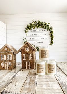 three candles sitting on top of a wooden table next to two small gingerbread houses