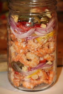 a glass jar filled with shrimp, onions and other vegetables on top of a table