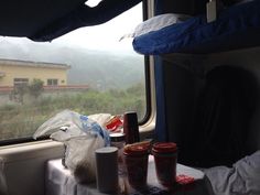 there are some food and drinks on the table in front of the window with mountains behind it