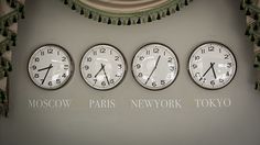 four clocks are hanging on the wall in front of a window with an inscription moscow paris new york