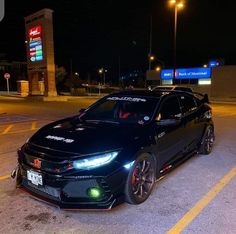 a black car parked in front of a gas station at night with its lights on