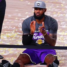 a basketball player sitting on the floor with his hands up in front of him and two other people standing behind him