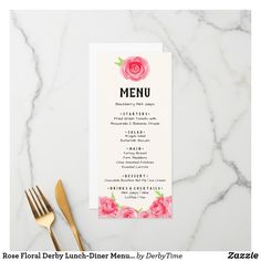 a menu card with pink flowers on it next to gold utensils and a fork