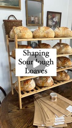 a wooden table topped with lots of loaves next to a shelf filled with bread