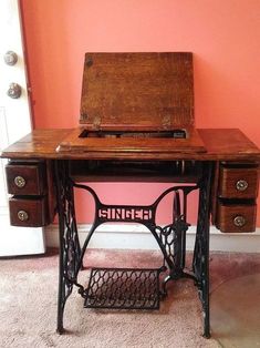 an old sewing machine sitting on top of a wooden table next to a pink wall