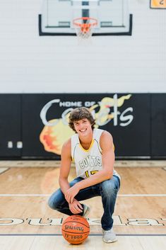 a young man kneeling down with a basketball in his hand on the court at a school gym