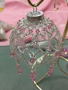 a pink ornament hanging from a gold stand on a table with other ornaments