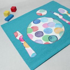 a colorful place mat with a spoon, fork and knife on it next to wooden blocks