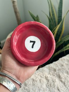 a person holding a red bowl with a white number seven on it in front of a potted plant