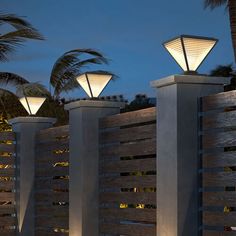 three lights on top of wooden posts in front of palm trees and fence at night