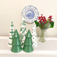 three ceramic christmas trees sitting on top of a table next to a vase filled with flowers