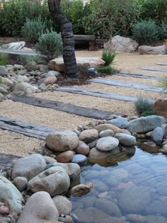 there is a small pond in the middle of this garden with rocks and gravel around it