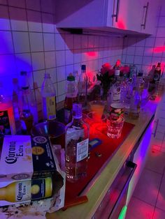 a kitchen counter covered in liquor bottles and other alcoholic items, with the lights on