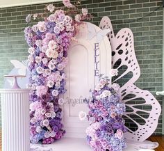 a white door surrounded by purple flowers in front of a brick wall