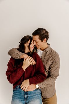 a man and woman hugging each other in front of a white wall