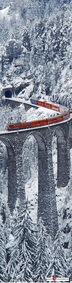 an orange train traveling over a bridge in the middle of snow covered hills and trees