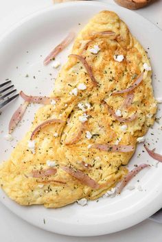 an omelet with ham and cheese is on a white plate next to bread