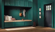 a room with green walls and wooden flooring has a bench, coat rack, and door