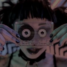 a woman holding up a cassette in front of her face with two hands on top of it