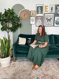 a woman sitting on top of a green couch next to a potted plant and clock