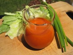 a glass pitcher filled with liquid sitting on top of a wooden cutting board next to lettuce