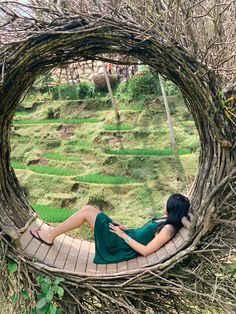 a woman laying down in a circular wooden structure with grass and trees around her, on the ground