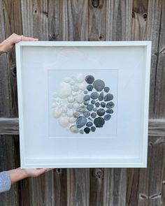 a person holding up a framed art piece with rocks in the shape of a heart