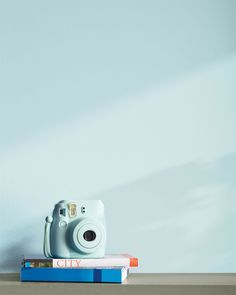 a white camera sitting on top of a stack of books next to a blue wall