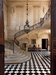 an ornate staircase with black and white checkered flooring in front of a chandelier