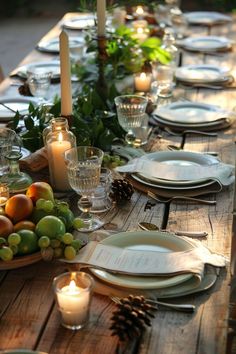 a table set with plates, candles and fruit on it for a festive dinner