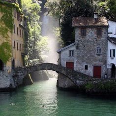 an old stone bridge over a river with buildings on both sides and water flowing under it