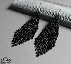 the black beaded fringe earrings are hanging from a silver hook on a gray background