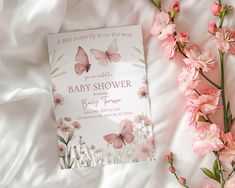 a baby shower book laying on top of a bed next to pink flowers and butterflies