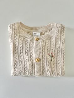 This sweet little sweater is machine knit (not handmade) but is hand embroidered by me. It is 100% organic cotton and available in size 6 months or 12 months. A beautiful creamy beige cable knit and hand embroidered with a delicate pink floral branch. Brand new.  Made in a smoke free and pet free environment. Cute Cotton Cable Knit Sweater, Cute Cream Cotton Cardigan, Cream Knit Sweater With Floral Embroidery, Cozy Cream Cotton Sweater, Beige Cotton Knitted Sweater, Beige Cotton Cable Knit Sweater, Beige Embroidered Cotton Cardigan, Embroidered Cream Cotton Sweater, Cream Cotton Embroidered Sweater