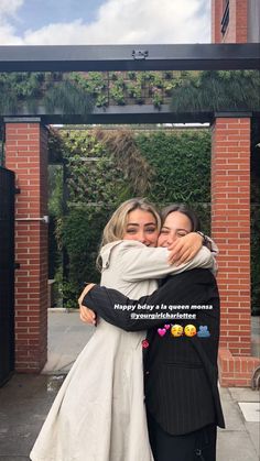 two women hugging each other in front of a building