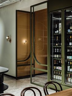 an empty table and chairs in a room with wine bottles on the wall behind glass doors