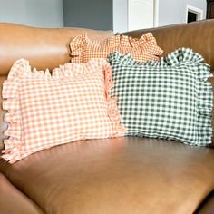 three pillows are sitting on the back of a brown leather couch in a living room