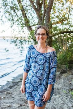 a woman wearing glasses and a blue dress is walking on the beach with trees in the background