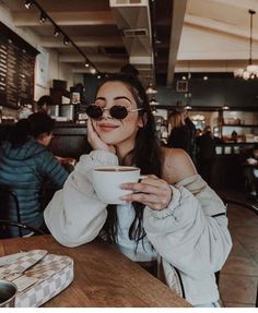 a woman sitting at a table holding a coffee cup