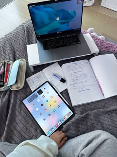 an open laptop computer sitting on top of a bed next to notebooks and pens