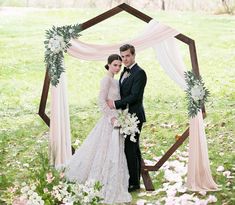 a bride and groom standing in front of an outdoor wedding ceremony arch with white flowers